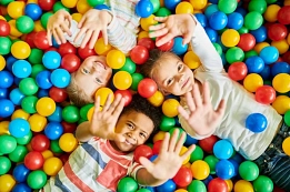 Kinder spielen im Bällebad Drei Kinder liegen in einem bunten Bällebad und winken in die Kamera. © Canva / Getty Images Pro