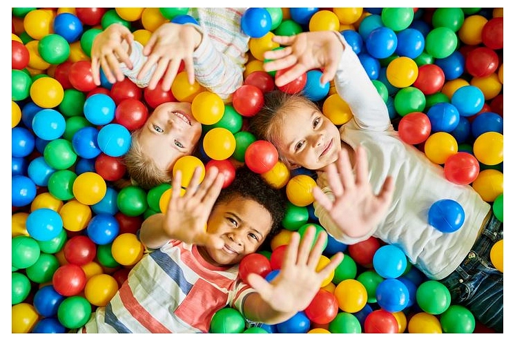 Drei Kinder liegen in einem bunten Bällebad und winken in die Kamera.&nbsp;&copy;&nbsp;Canva / Getty Images Pro