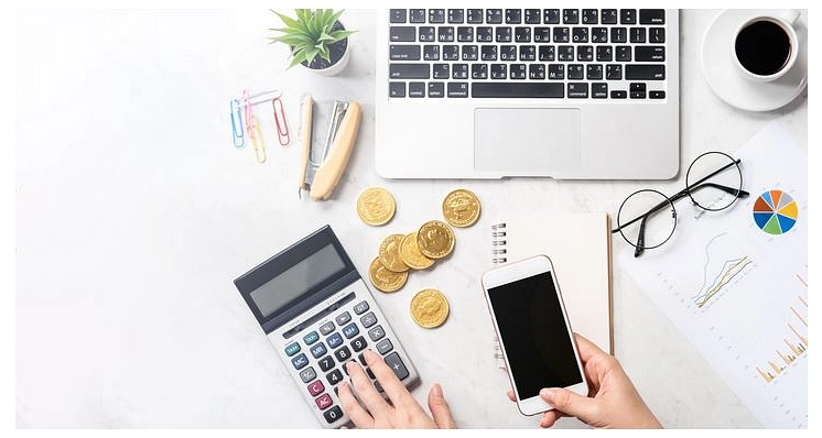 Schreibtisch mit Laptop, Taschenrechner, Münzen, Smartphone und Diagrammen.&nbsp;&copy;&nbsp;Canva
